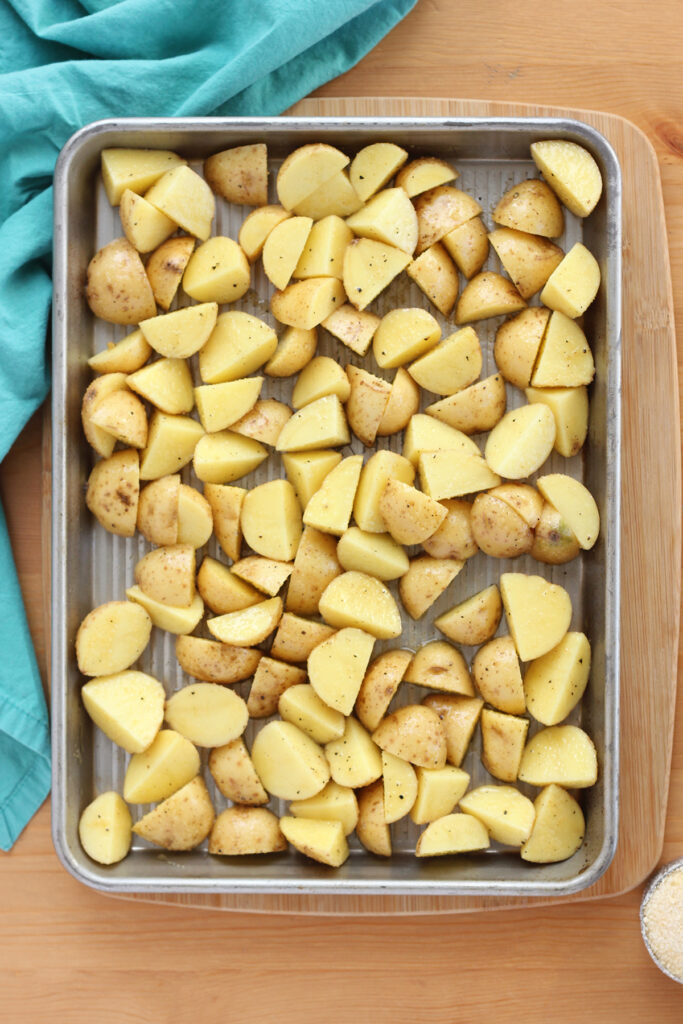 top down image showing a sheet pan spread with uncooked potatoes that have been cut and seasoned 