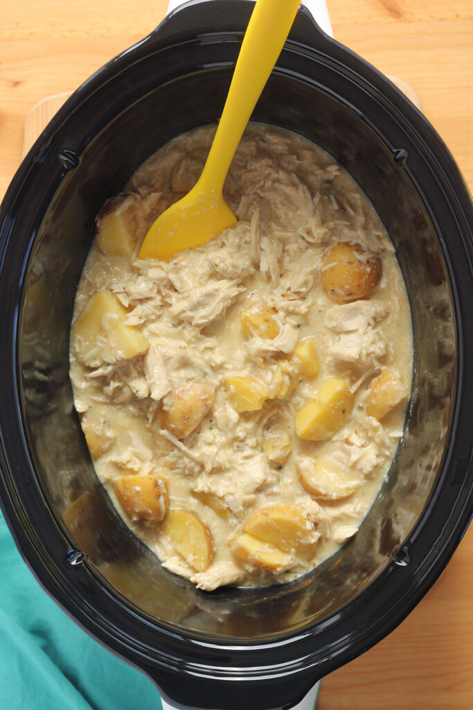 top down image showing the inside of a slow cooker filled with shredded chicken and potatoes with a soup mixture