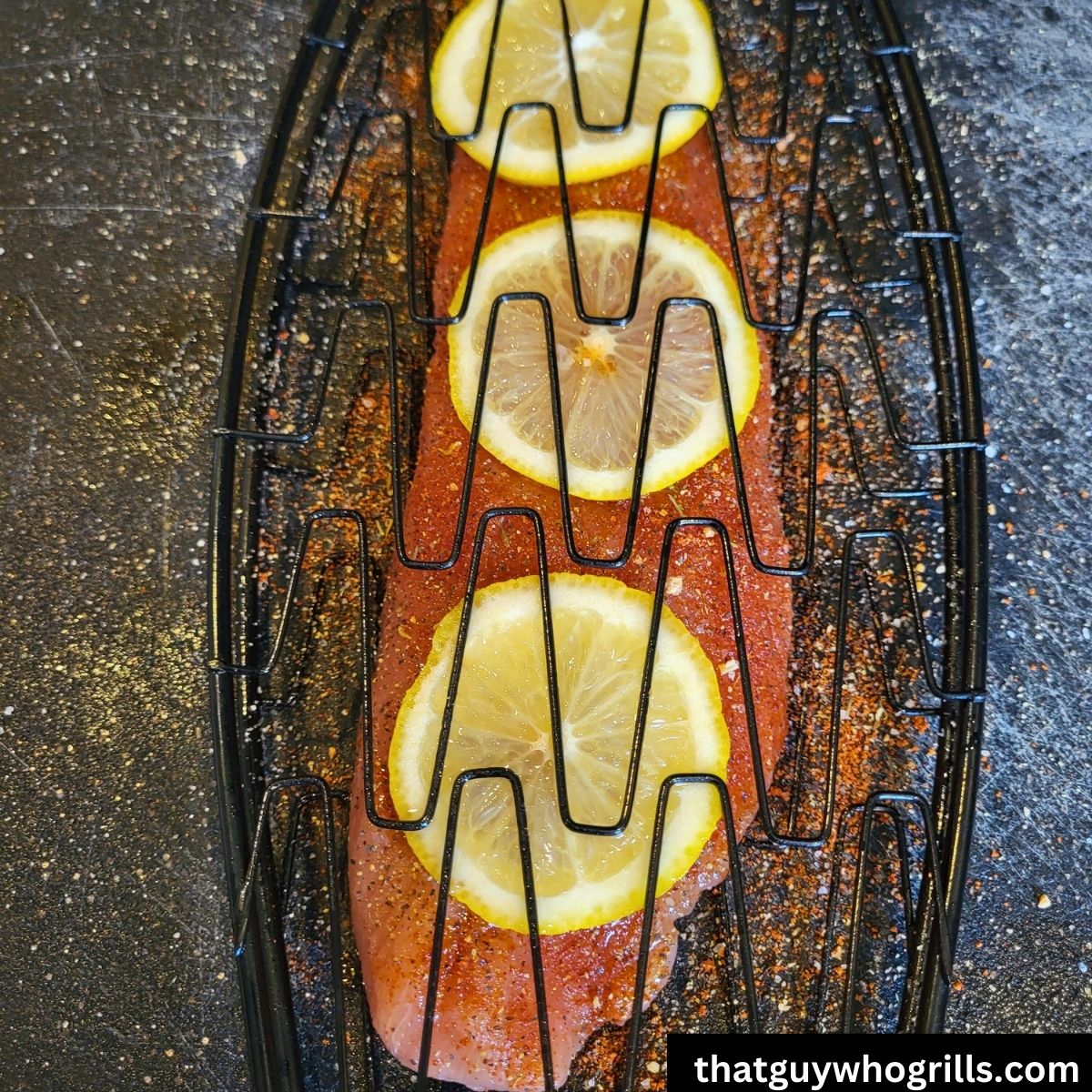 Salmon fillet seasoned with lemon slices in fish basket before grilling