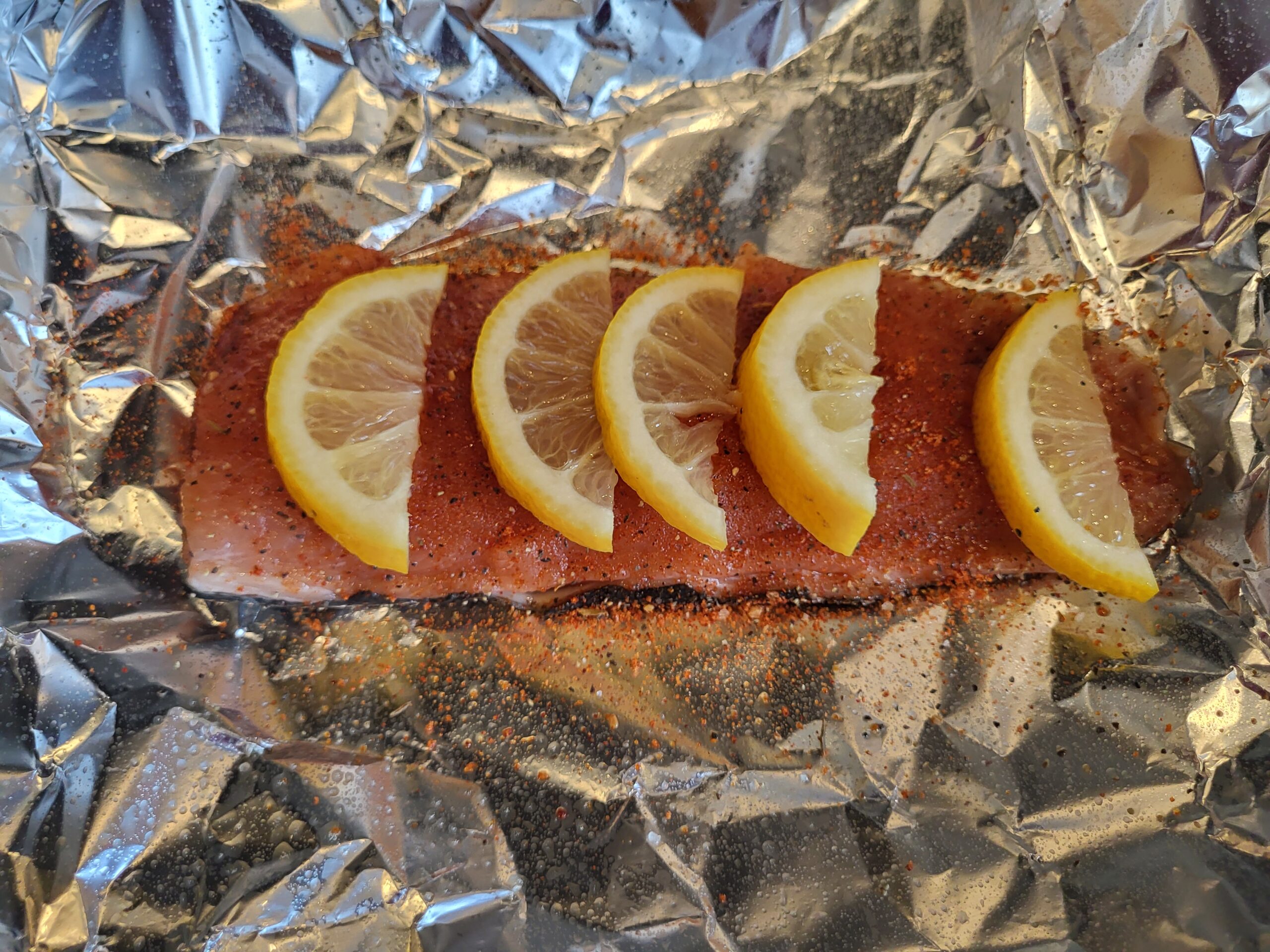 Salmon fillet on foil seasoned with lemon wedges