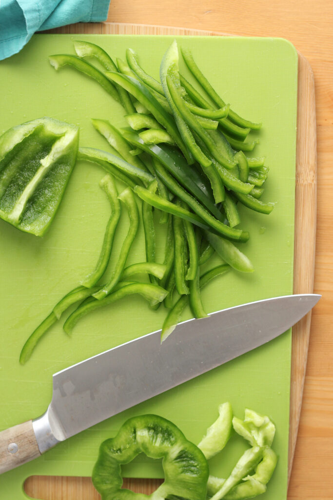 top down image showing a green cutting board with slices of green bell pepper and a chef knife