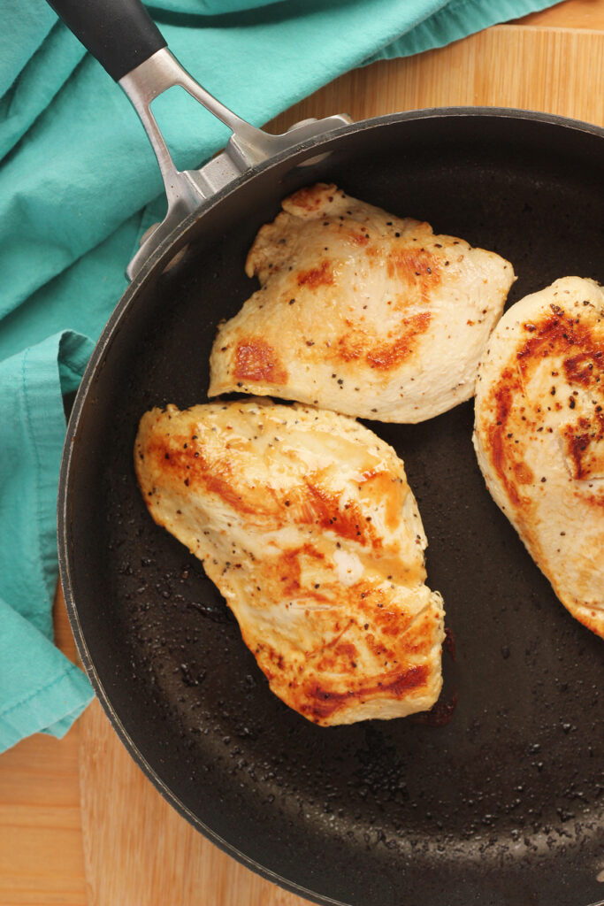 Top down image showing a black skillet with three golden brown chicken breasts sitting inside 