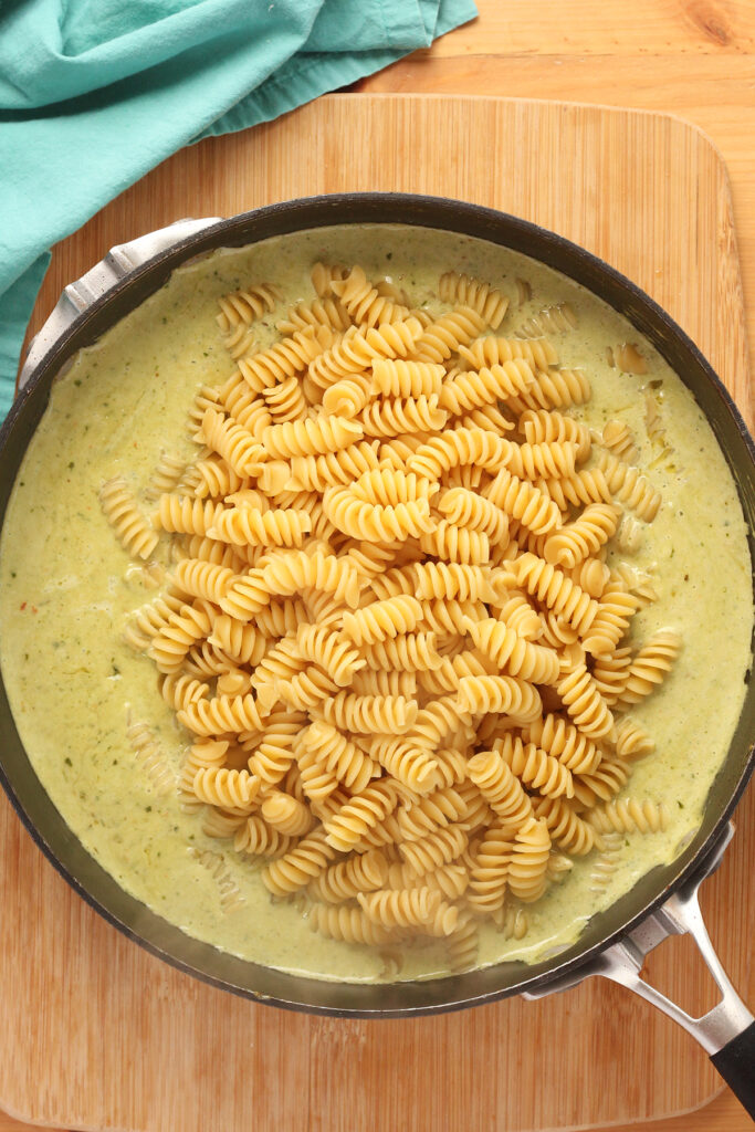 top down image showing a deep black skillet filled with a green sauce with cooked rotini pasta on top